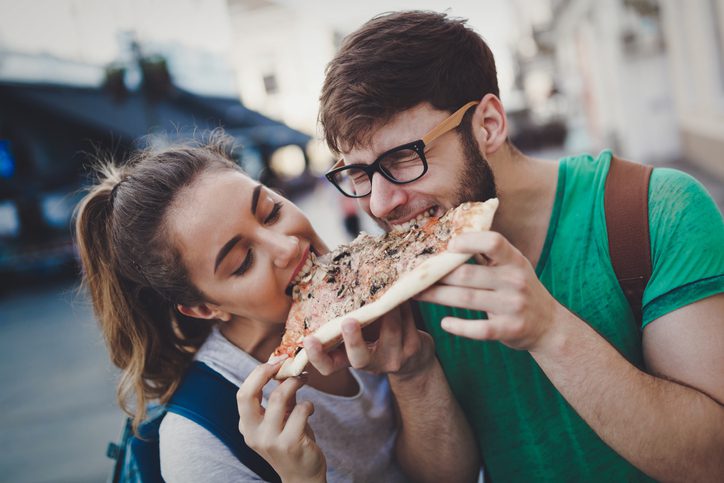 a man and a woman sharing a bit of a giant piece of pizza