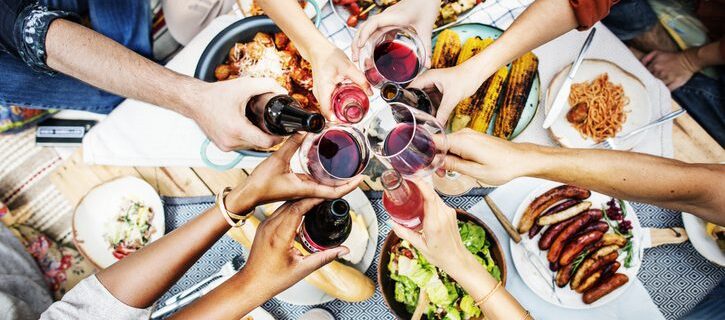 seven people clinking glasses of red wine or beer bottle over a barbeque picnic table