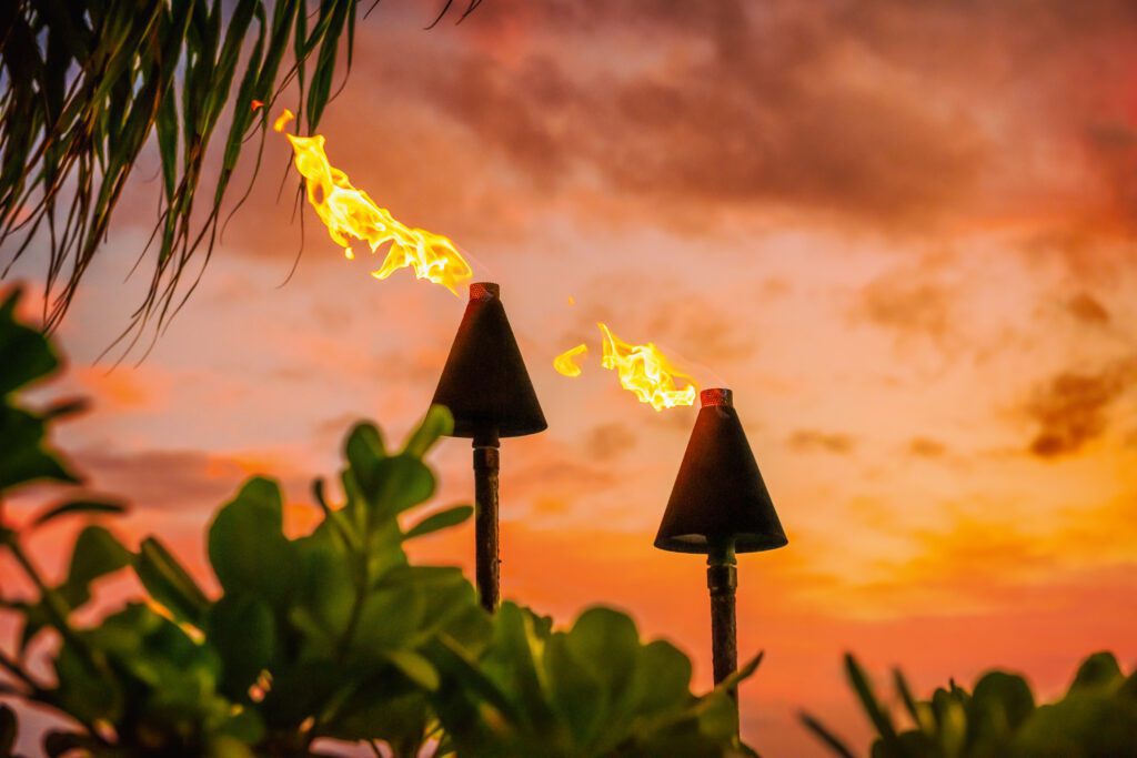 Hawaii luau party Maui fire tiki torches with open flames burning at sunset sky clouds at night. Hawaiian cultural travel vacation background.